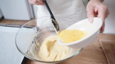 Beyaz önlüklü kadın çırpılmış yumurtayı hamurla birlikte ağır çekimde tabağa döküyor..