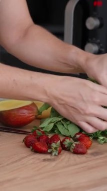 Beyaz önlüklü kadın pasta şefi eklerleri hazırlıyor. Bir nane yaprağı seçiyor ve pastayı yavaş çekimde incelikle süslüyor. Dikey video.