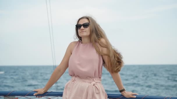 一位年轻女子站在船的上层 穿着飘逸的粉色衣服 长发在蓝天的背景下迎风摇曳 慢动作 — 图库视频影像