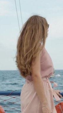 Bir yolcu gemisindeki genç bir kadın üst güvertede duruyor, bana doğru dönüyor, şehir arka planda kayalıklarla çevriliyken. Ağır çekim. Dikey video.