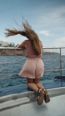 Genç kadın, geminin güvertesinde diz çöküyor, korkuluklara tutunuyor. Saçları ve kıyafetleri rüzgarla savruluyor, ağır çekimde. Dikey video.