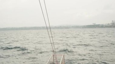 Geminin pruvası çalkantılı bir denizin arka planında şehre doğru yelken açıyor. Hava bulutlu..