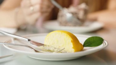 Yarım limonlu krema tabağı ve arka planda tatlısını yiyen bir kadın..