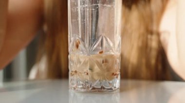 Güneşli bir günde, bir kadın bir kafede pipetle milkshake içiyor. Güneş ışınları arkasından onun üzerinde parlıyor. Yakın plan..