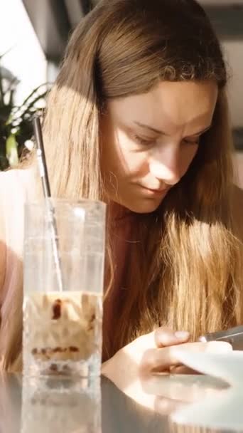 Młoda Kobieta Kawiarni Patrzy Swojego Smartfona Niedokończonym Koktajlem Talerzami Stole — Wideo stockowe