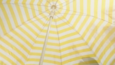 Beyaz ve sarı çizgili bir plaj şemsiyesi güneşten uzak durur..