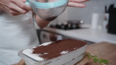 Bir kadın ağır çekimde tiramisu kekinin üstüne kakao tozu serpiyor..