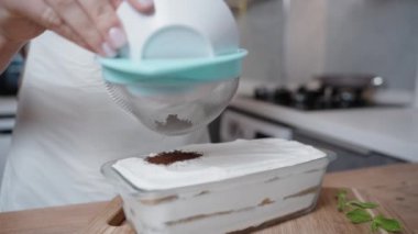 Bir kadın tiramisu kekinin üzerindeki kakao tozunu yavaş çekimde süzgeçten geçirir. Yakın çekim..