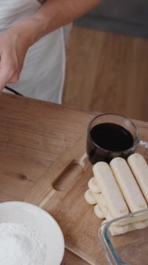 Tiramisu için beyaz krema çırpan bir şefin tepeden tırnağa görüntüsü. Pasta için çeşitli malzemeler masaya serildi. Dikey video.