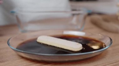 Kadın Savoiardi bisküvilerini kahveye bandırıyor ve onları bir pasta tabağına aktarıyor..