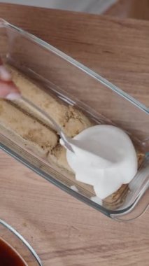 Tiramisu keki hazırlıklarına tepeden tırnağa bir bakış. Kadın kremayı Savoiardi bisküvilerinin üzerine yayıyor. Dikey video.