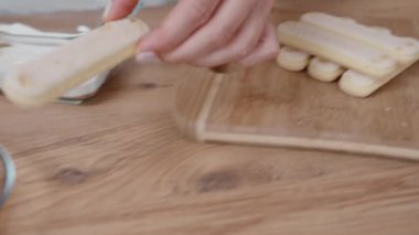 Pasta şefi bir parça Savoiardi bisküvisi alıyor, kahveye bandırıyor ve beyaz kremanın üzerine yerleştiriyor. Eylem ağır çekimde çekilir..