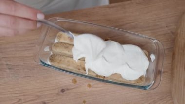 Kadın beyaz kremayı Savoiardi bisküvisinin üzerine yayıyor..