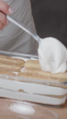 Kadın son krema tabakasını Savoiardi bisküvilerinin üzerine serer. Tiramisu keki neredeyse hazır. Dikey video.