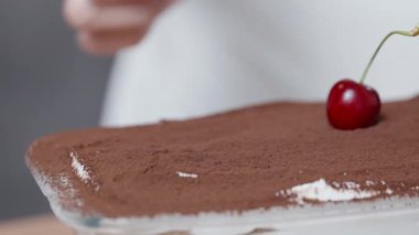 Ağır çekimde, pasta şefi tiramisu kekini kirazla süslüyor. Yakın plan..