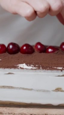 Kadın, Tiramisu pastasının tepesini süsleyen kirazdan sapları çıkarıyor. Dikey video.