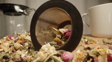 Çay seremonisi, çiçek çayı ve gül yapraklarıyla dağılmış dağınık bir masa. Masadan çay süzgeciyle çay süzgecini aldım. Dolly kaydırıcı aşırı yakın çekim.