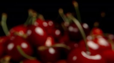 Siyah bir zemin üzerinde olgun kiraz kümesi, odak yavaşça uzaklığa doğru hareket ediyor ve kayboluyor..