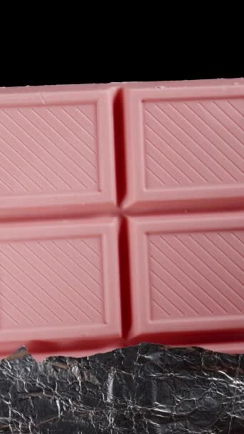Півзагорнутий Рожевий Шоколадний Батончик Вкритий Блискучою Фольгою Обертається Чорному Тлі — стокове відео