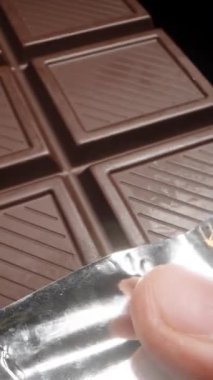 Elimde tutuyorum ve siyah arka planda büyük siyah bir çikolatayı yakından inceliyorum. Dikey video.