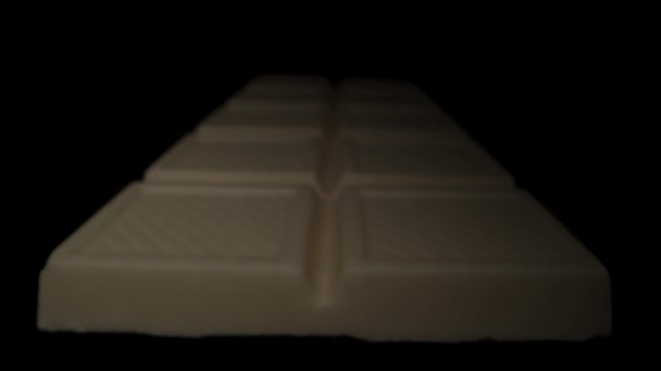 カットアウトのための黒い背景にあるホワイトチョコレートバー 光はさまざまな角度からそれを照らします クローズアップ — ストック動画