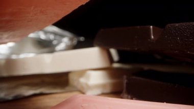 Siyah arka plana ve ahşap masaya farklı renkte çikolatalar yerleştirilmiş. Dolly kaydırıcı aşırı yakın çekim.