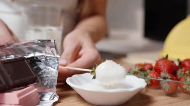 Kadın beyaz çikolata kaplı, hindistan cevizi gevreğiyle çilekleri yuvarlıyor. Yavaş çekim.