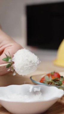 Kadın hazır çilekleri beyaz çikolata ve hindistan cevizli şiş üzerine koyar. Dikey video.