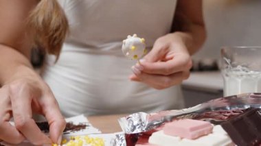 Kamera yavaşça yaklaşırken kadın çilekleri renkli şeker toplarıyla beyaz çikolatayla süslüyor..