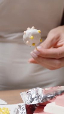 Kamera yavaşça yaklaşırken kadın çilekleri renkli şeker toplarıyla beyaz çikolatayla süslüyor. Dikey video.