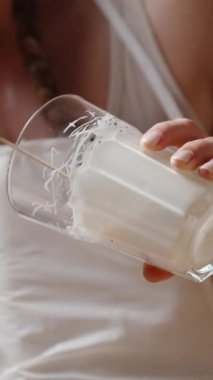 Kadın çileği bir bardak beyaz çikolataya bandırıyor, halihazırda süslenmiş çilekleri de yakınlarda duruyor. Ağır çekim. Dikey video.