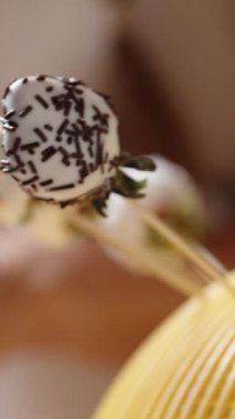 Kamera, çikolataya batırılmış çilek yerine çikolatacı birinin üstüne hindistan cevizi serptiği ana odaklanıyor. Ağır çekim. Dikey video.