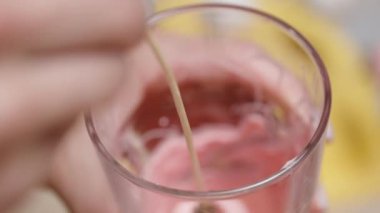 Yavaş çekimde, bir çilek bir bardak pembe çikolataya batırılıyor ve sonra fazla çikolatanın damlamasına izin vermek için dışarı çıkarılıyor. Kapat.