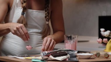 Örgülü saçlı bir kadın çilekleri pembe çikolatayla süslüyor, şeker parçacıkları kullanıyor. Yavaş çekim.