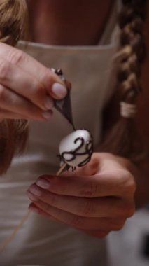 Kadın çilekleri beyaz çikolatayla süslüyor. Boru çantasındaki siyah çikolatayla karışık desenlerle. Ağır çekim. Dikey video.