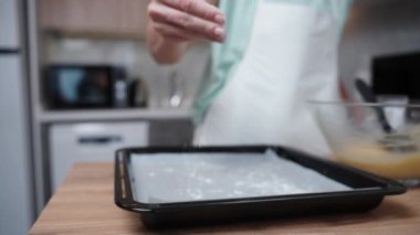 Kadın, ağır çekimde, elinden fırın çarşafına un serpiştiriyor, yakın plan..