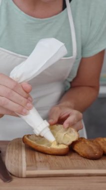 Kadın pasta poşetindeki eklere krema sıkıyor, ağır çekimde. Dikey video.