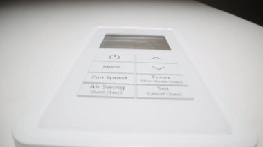 Bir kadının parmağı, beyaz klimanın uzaktan kumandasındaki güç düğmesine basar. Dolly kaydırıcı aşırı yakın çekim.