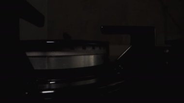 Mutfaktaki siyah bir gaz sobasının yakın plan fotoğrafı. Dairesel bir şablonla karanlıkta aydınlatılmış..