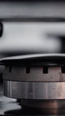 Siyah bir ocağın üzerinde temiz bir gaz ocağının yakın çekim görüntüsü ve üzerine bir tencere konmuş ve ateş yanıyor. Dikey video.