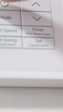 Kadın klimayı açıyor ve yakın plan çekimde beyaz kumandanın ısısını düşürüyor. Dikey video.