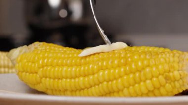 Yavaş çekimde, bir çatal, pişmiş mısırın üzerine yayılan bir parça tereyağı tutar..