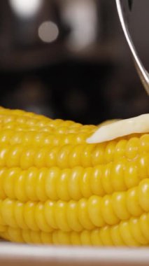 Dikey video. Yavaş çekimde, bir çatal, pişmiş mısırın üzerine yayılan bir parça tereyağı tutar..