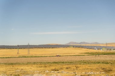 Çöl manzarasında güneş panelleri, tarlayı traktörle süren çiftçiler, arka planda dağlar..