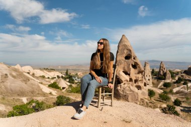 Genç bir kadın, yüksek bir tepedeki sandalyede antik uçurum evlerinin arka planında oturuyor. Türkiye 'de Seyahat.