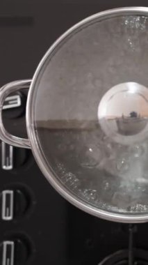 Dikey video. Kendimi yanıklardan korumak için kırmızı fırın eldiveni kullanarak tencerenin kapağını kaynar suyla kaldırıyorum. Manzara yukarıdan ve sahne yavaş çekimde..