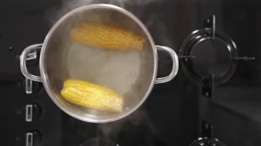 İki mısır tanesinin kaynadığı siyah gaz sobasının tepesinden aşağı bakan manzarası..