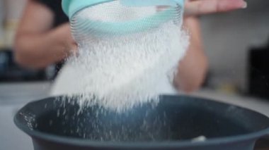 Mutfakta bir kadın, unu süzgeçten geçirip mavi bir kâseye sokuyor. Yavaş çekim, yakın çekim..