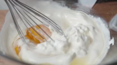 Bir kadın yavaş çekimde yumurta, süzme peynir ve krem çırpar..
