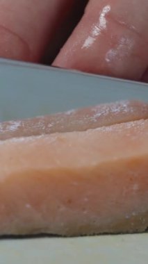 Dikey video. Bir kadın somon derisini yüzüyor. Yakın plan..